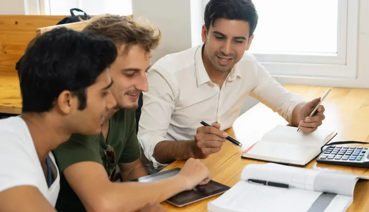 Três estudantes conversando e estudando juntos, com livros e materiais de estudo sobre a mesa, representando a oportunidade de aprendizado oferecida pelos cursos técnicos e superiores do IFMG.