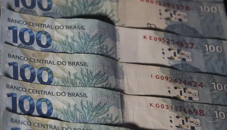 Notas de 100 reais empilhadas representando liberação de saques pela Caixa.
