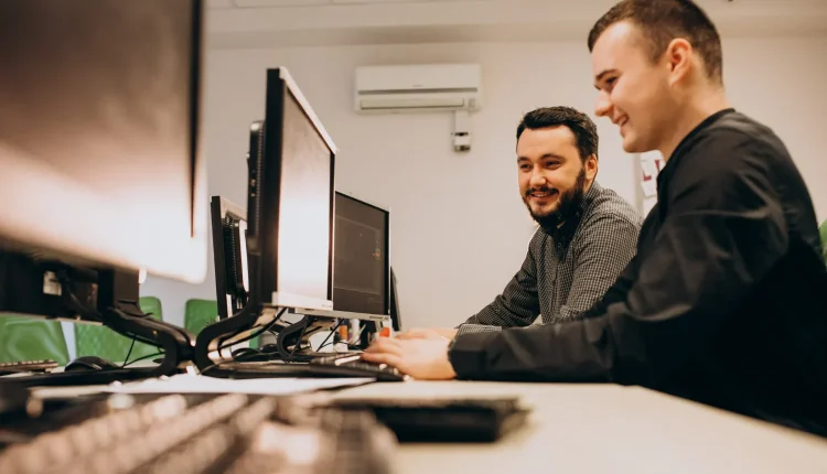 Dois jovens profissionais trabalhando juntos em computadores em um ambiente de escritório.