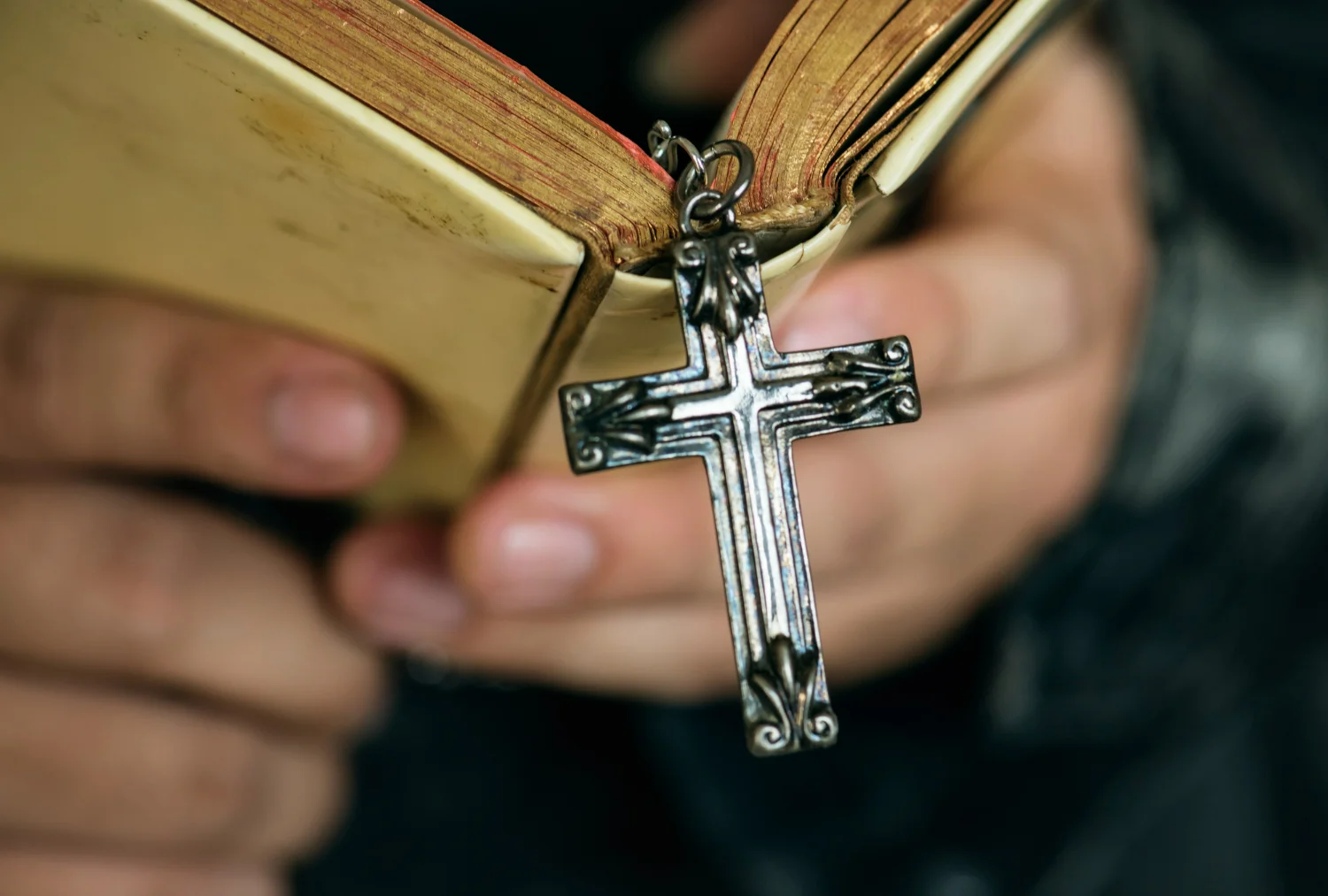 Detalhe de uma cruz metálica pendurada em uma Bíblia, simbolizando a origem cristã da palavra 'cristão'.