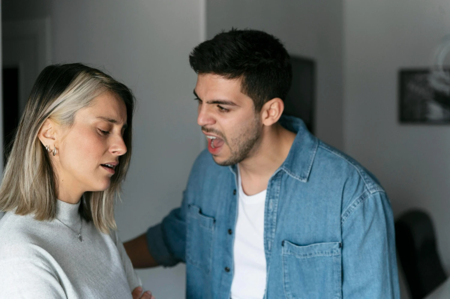 Homem falando com expressão de raiva para uma mulher que parece triste e desconfortável.
