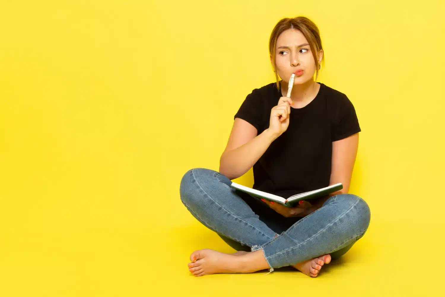 Mulher sentada com um livro na mão, pensativa e com um gesto de dúvida, ilustrando a confusão sobre 'Deus te abençoe' ou 'Deus te abençõe'.