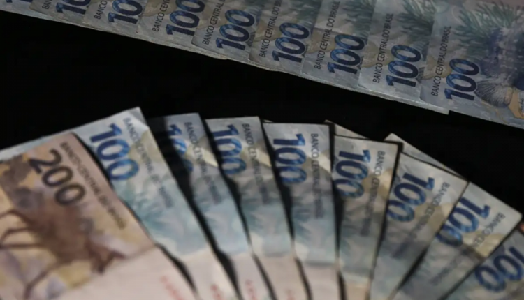 Notas de dinheiro brasileiro, incluindo várias cédulas de 100 reais e uma de 200 reais, dispostas sobre fundo preto.
