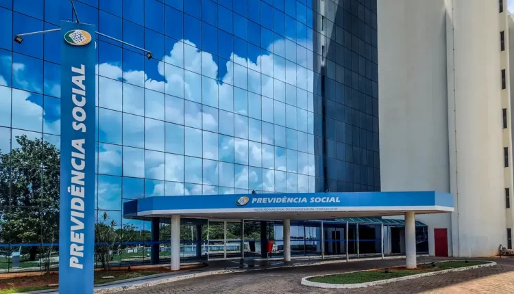 Fachada moderna do prédio da Previdência Social refletindo céu azul com nuvens.