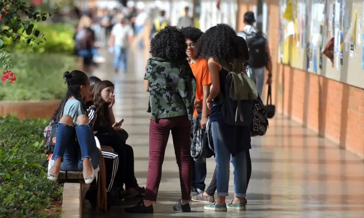 Grupo de estudantes em um corredor universitário conversando e interagindo em ambiente acadêmico.