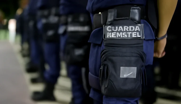Guardas municipais em formação, com destaque para a bolsa tática com o nome 'GUARDA MUNICIPAL', em um ambiente noturno.