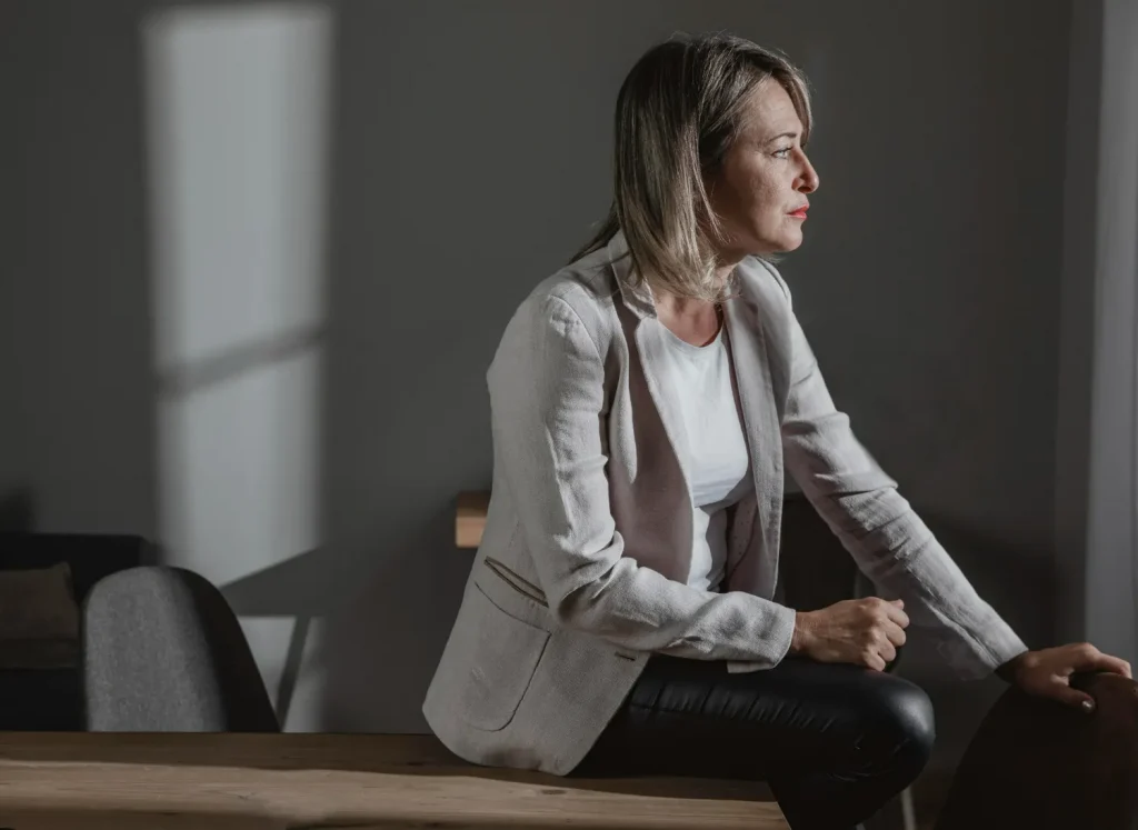 Mulher de meia-idade sentada pensativa em ambiente escuro, representando os efeitos emocionais da solidão.