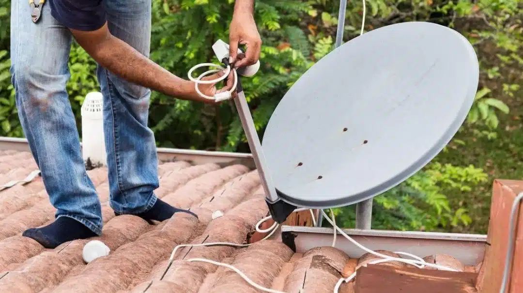 Instalação de antena parabólica em telhado residencial por um técnico.
