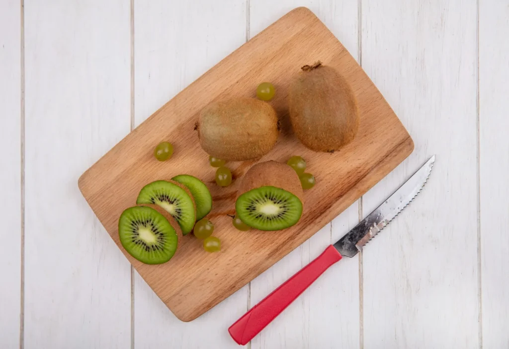 Kiwi fatiado em uma tábua de corte com uvas e uma faca ao lado.