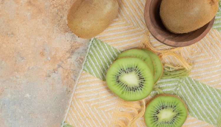 Kiwi cortado em fatias finas, disposto sobre um pano colorido com uma peça inteira ao lado.