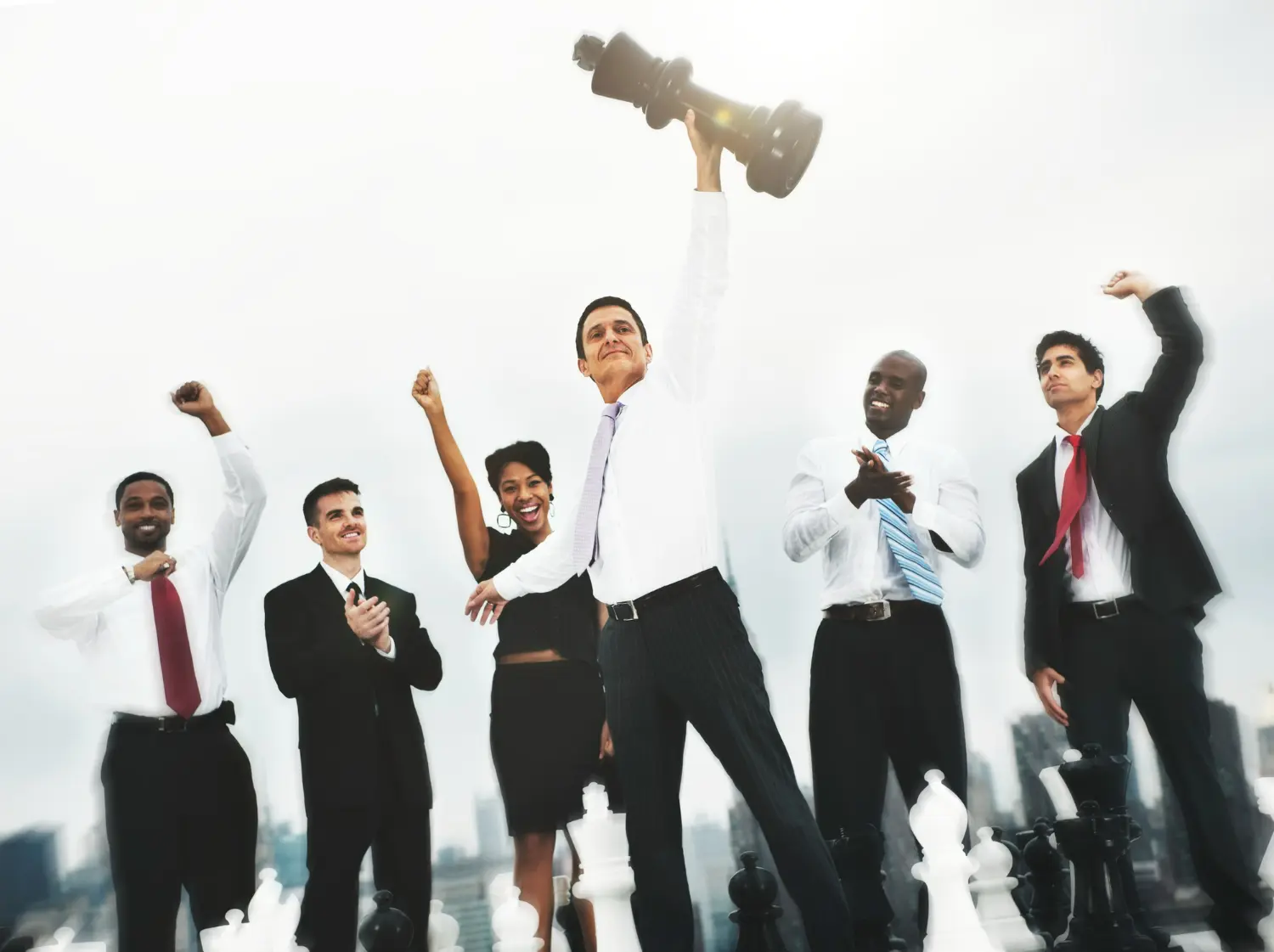 Equipe celebrando uma conquista juntos, com o líder segurando um grande peão de xadrez, simbolizando o trabalho em equipe e a colaboração.