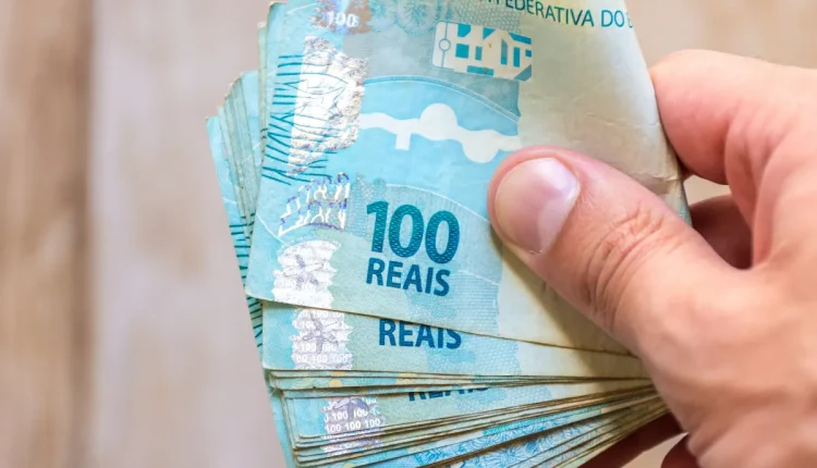Mão segurando várias notas de 100 reais.