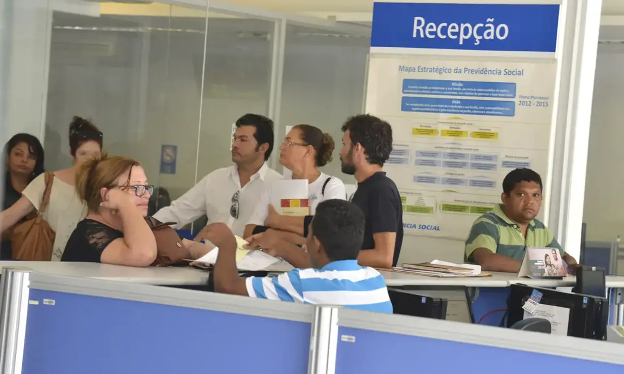 Atendimento em uma agência do INSS, com beneficiários sendo atendidos na recepção.