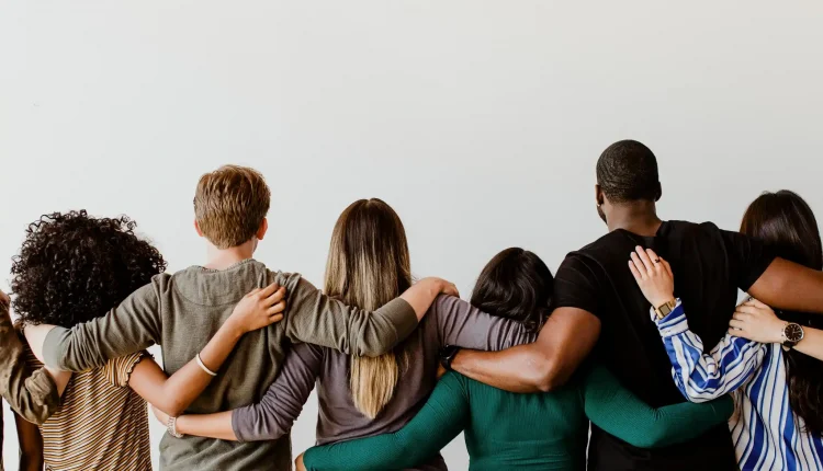 Grupo diverso de pessoas abraçadas, mostrando união e amizade.