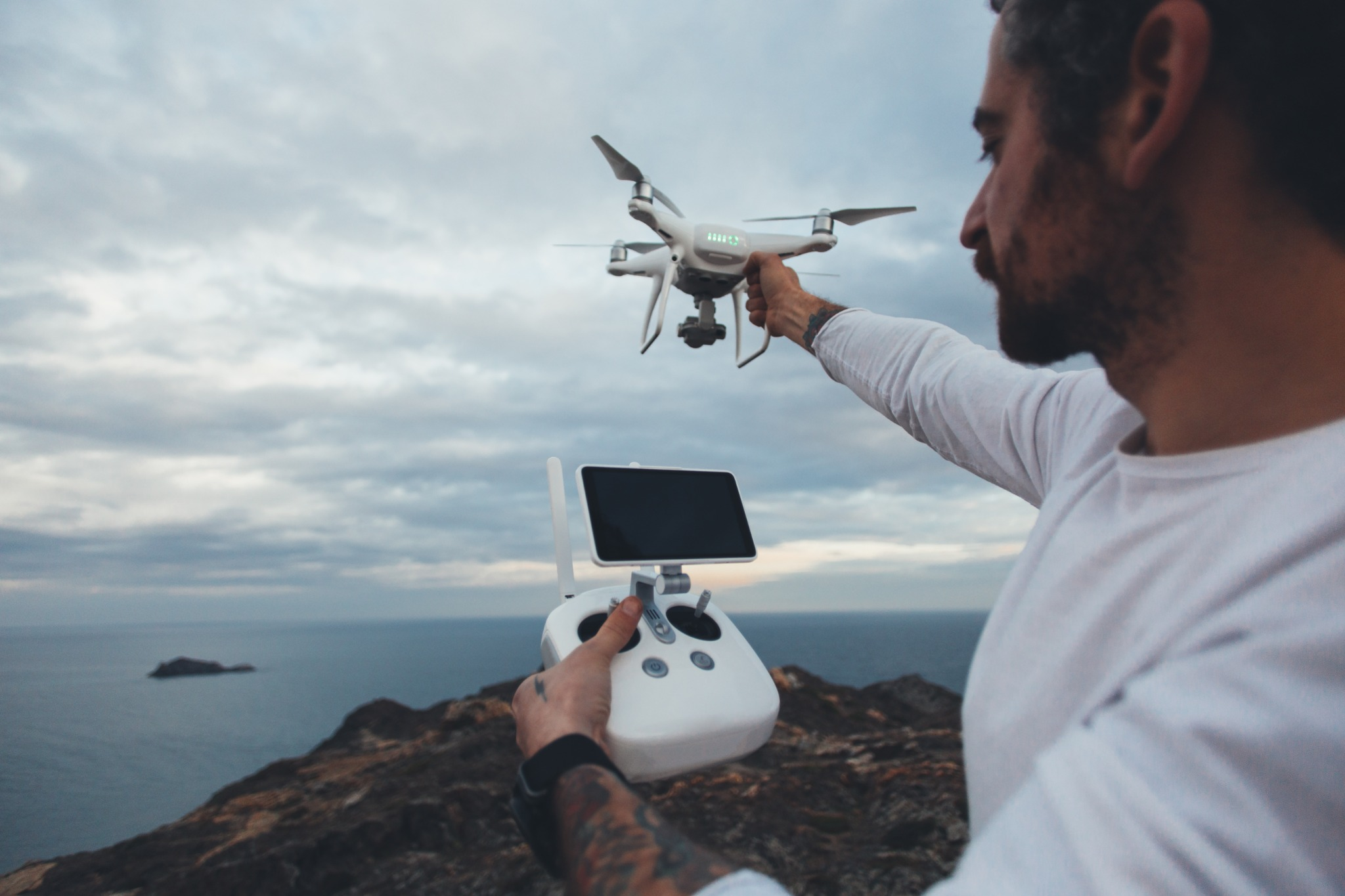 Operador segura drone e controle remoto à beira-mar.