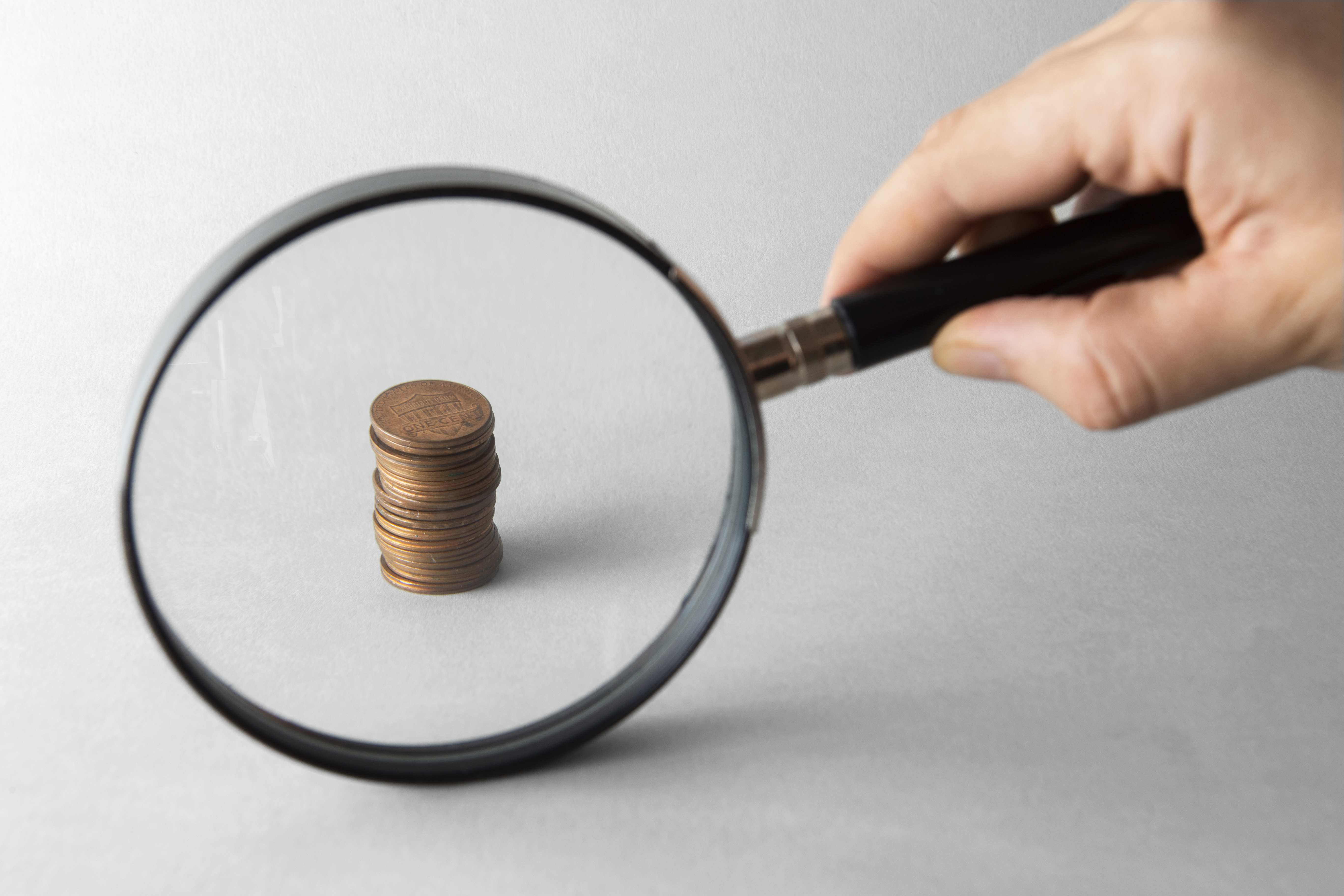 Lupa ampliando pilha de moedas em fundo cinza, destacando processo de análise