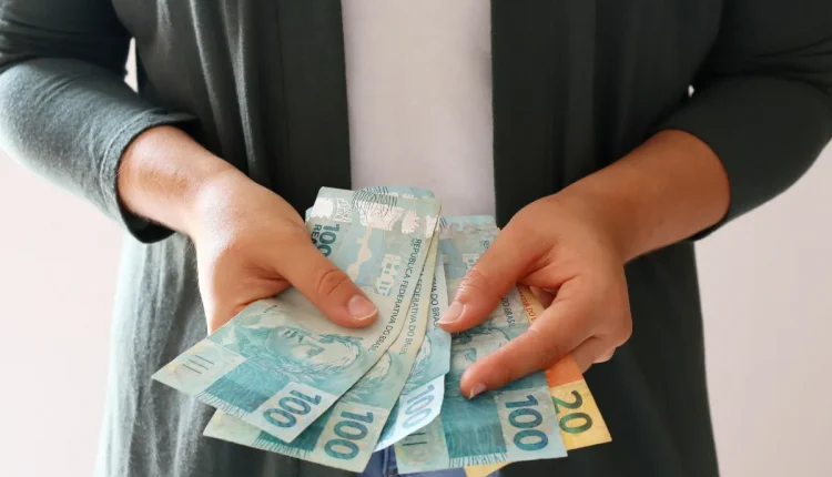 Pessoa segurando notas de R$100 e R$20, representando dinheiro em espécie.