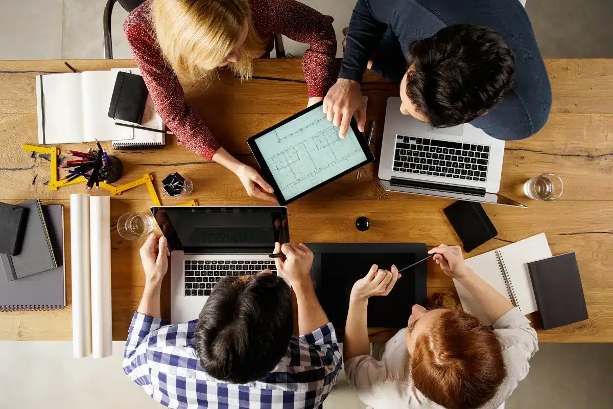 Equipe reunida em mesa de trabalho analisando projetos digitais.