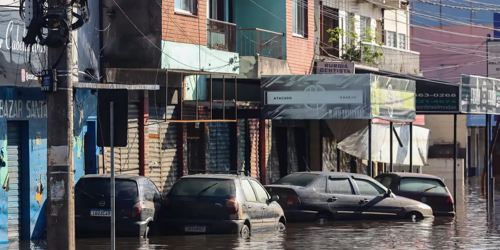 Rua com carros submersos após enchente em área urbana.