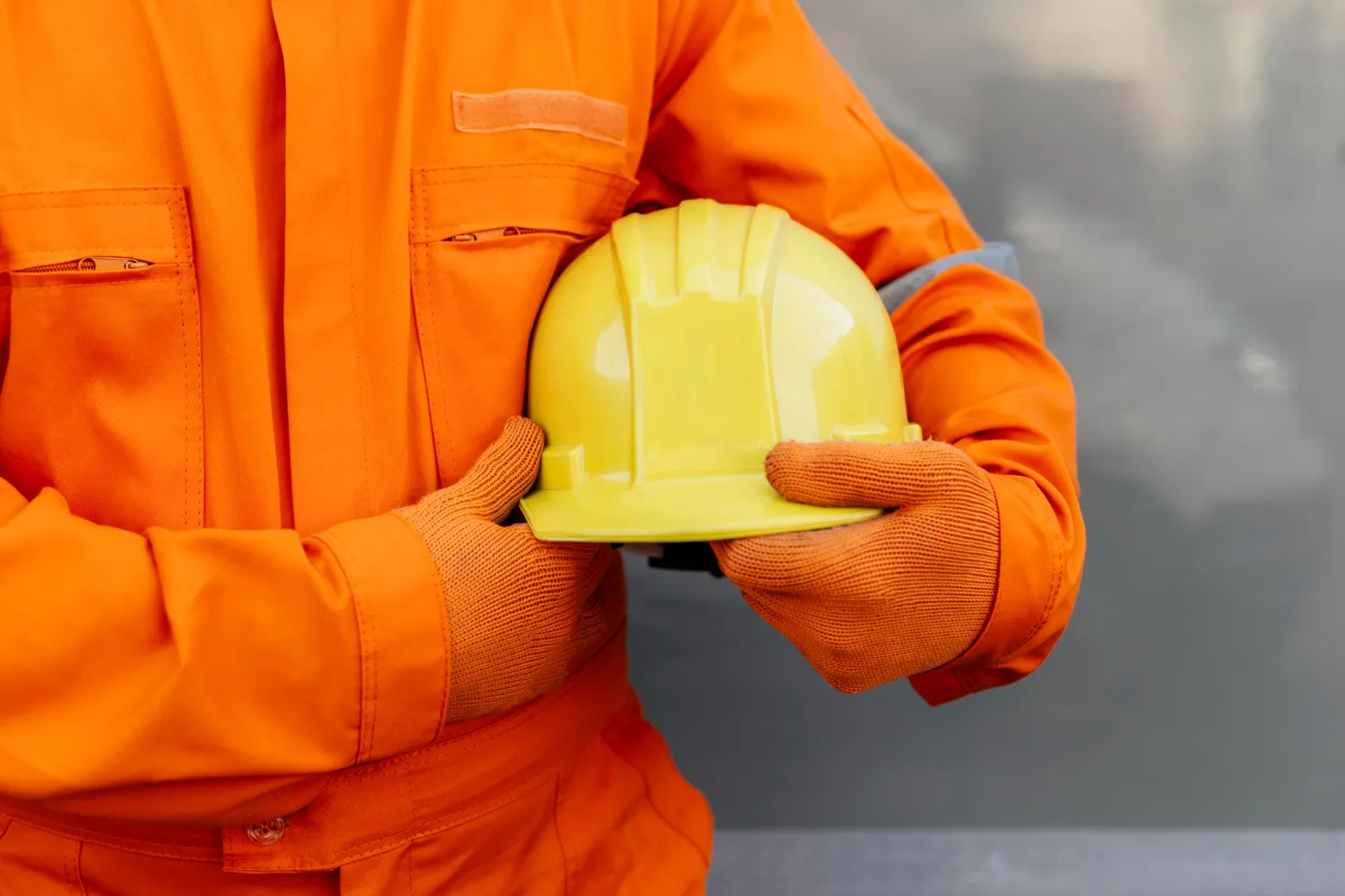 Profissional de segurança do trabalho segurando um capacete amarelo, com uniforme de proteção.