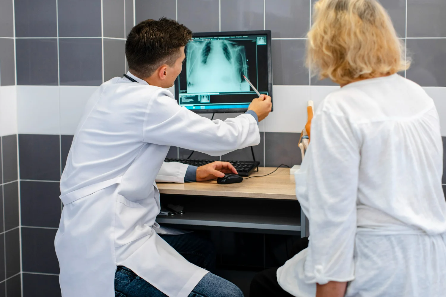 Técnico em radiologia explicando exame de raios-X para paciente em consultório médico.