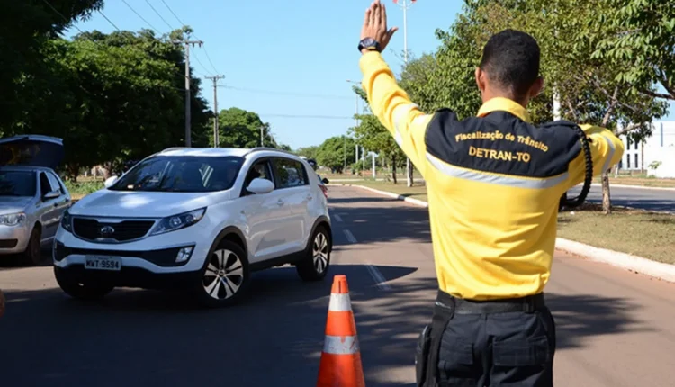 Agente de trânsito orientando o tráfego com cone, representando fiscalização do DETRAN-TO.