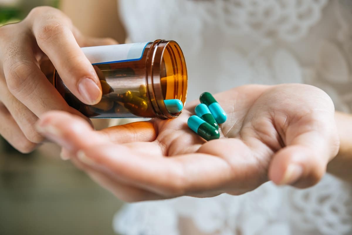 Pessoa segurando frasco de medicamentos com cápsulas.