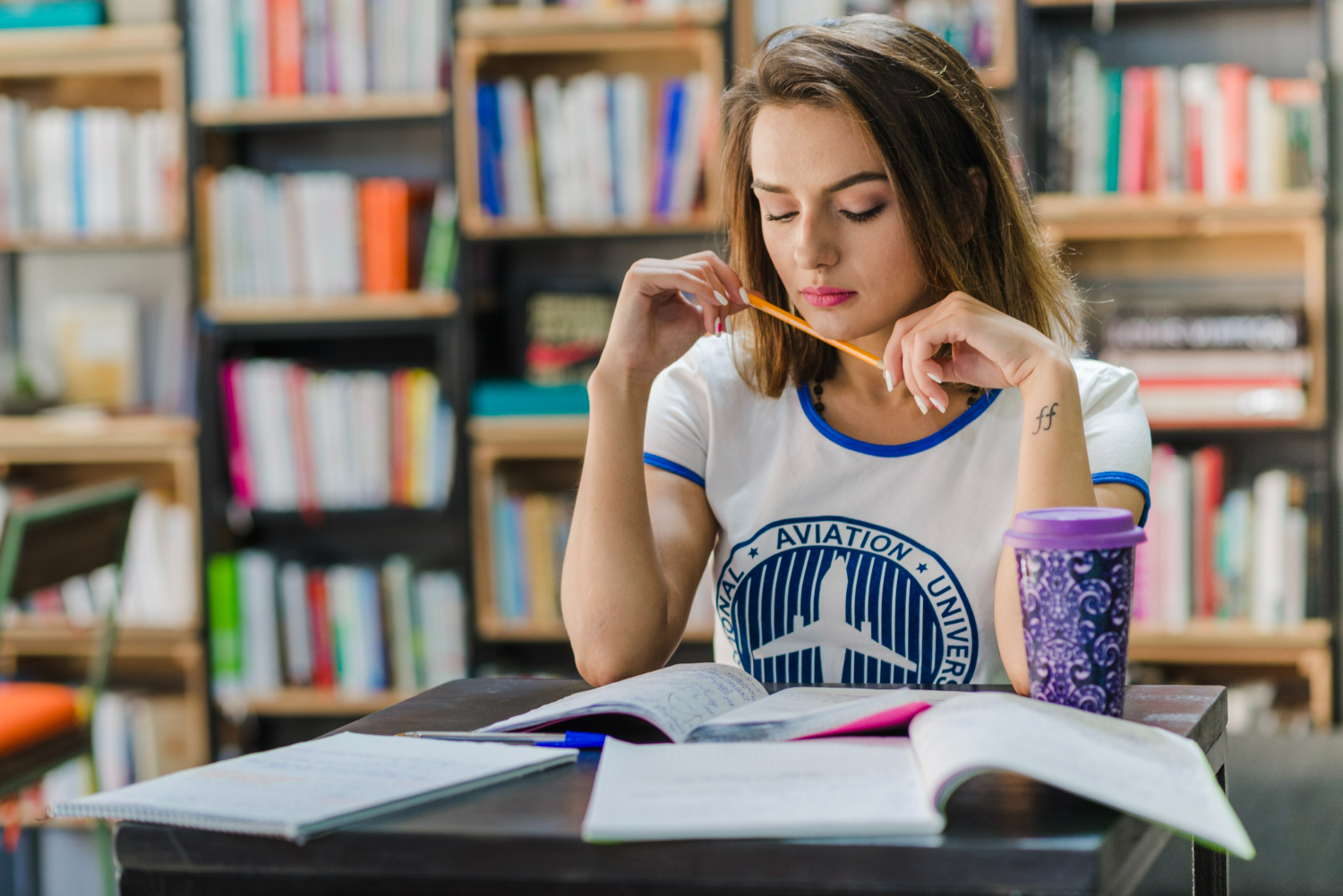 Mulher estudando em uma mesa com livros e lápis, focada na redação.