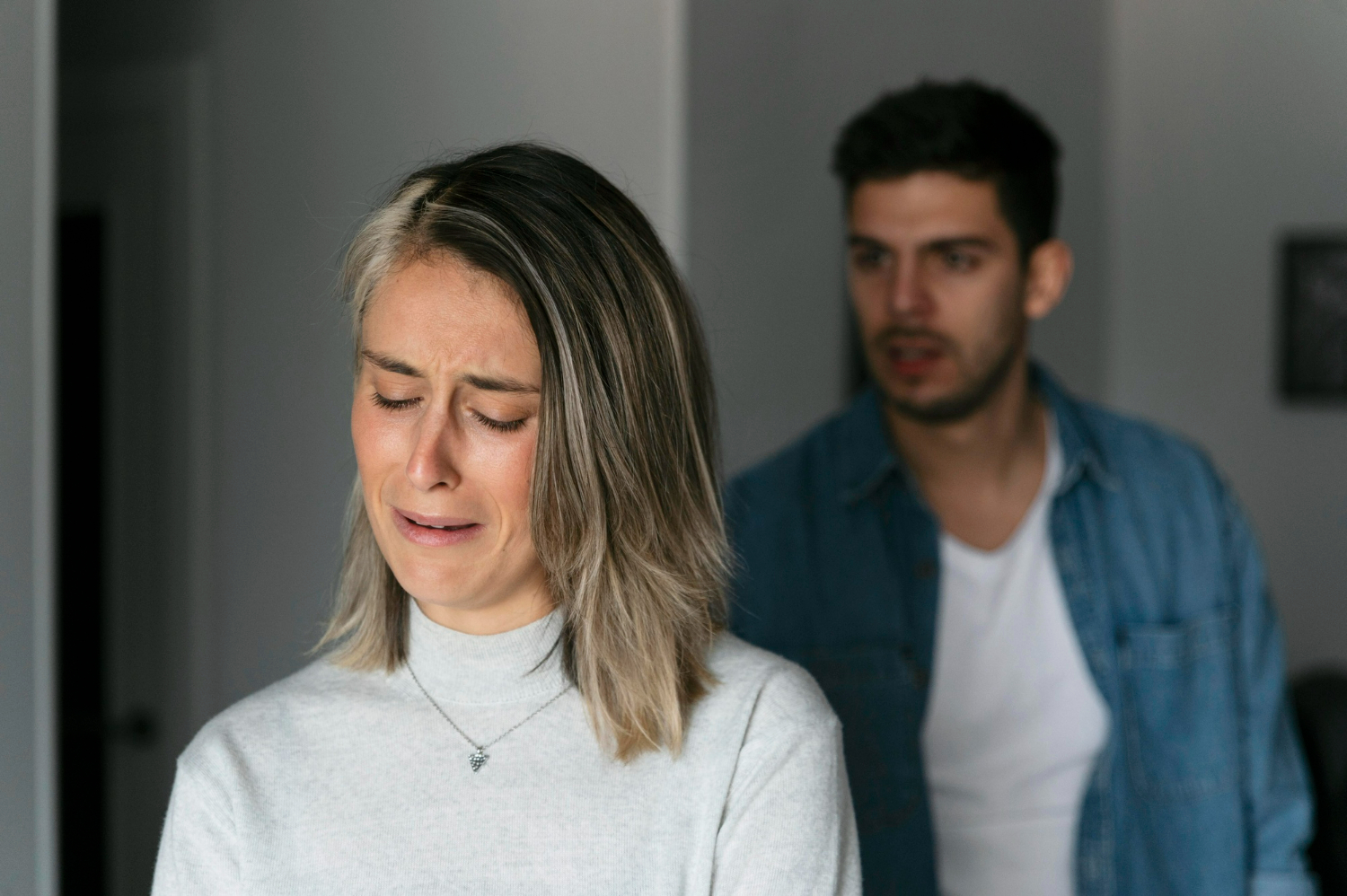 Mulher chorando enquanto um homem a observa, ambos em um momento de conflito emocional.