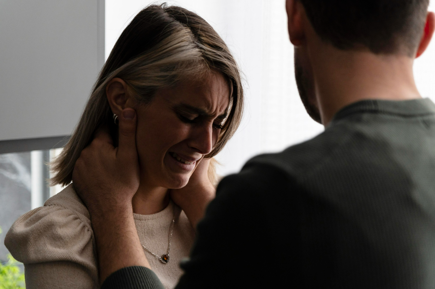 Mulher com expressão de dor e lágrimas, enquanto um homem a segura pelo pescoço.