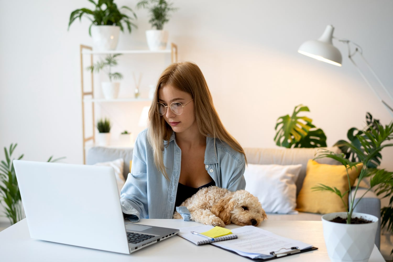 Mulher organizando seu espaço de trabalho em casa, com um cachorro descansando ao lado e uma mesa bem arrumada.