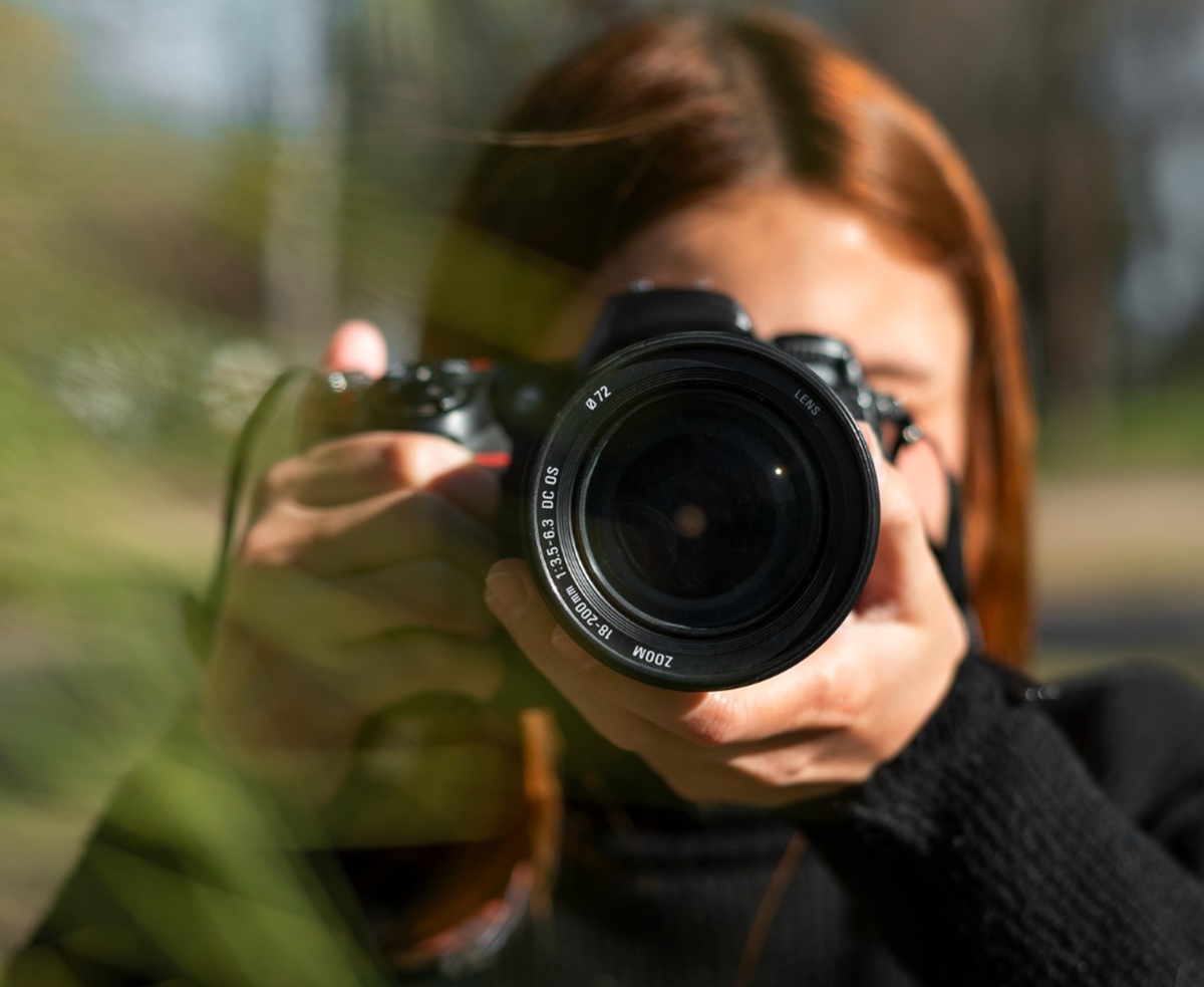 Fotógrafo segurando câmera reflex, focando no seu objetivo.