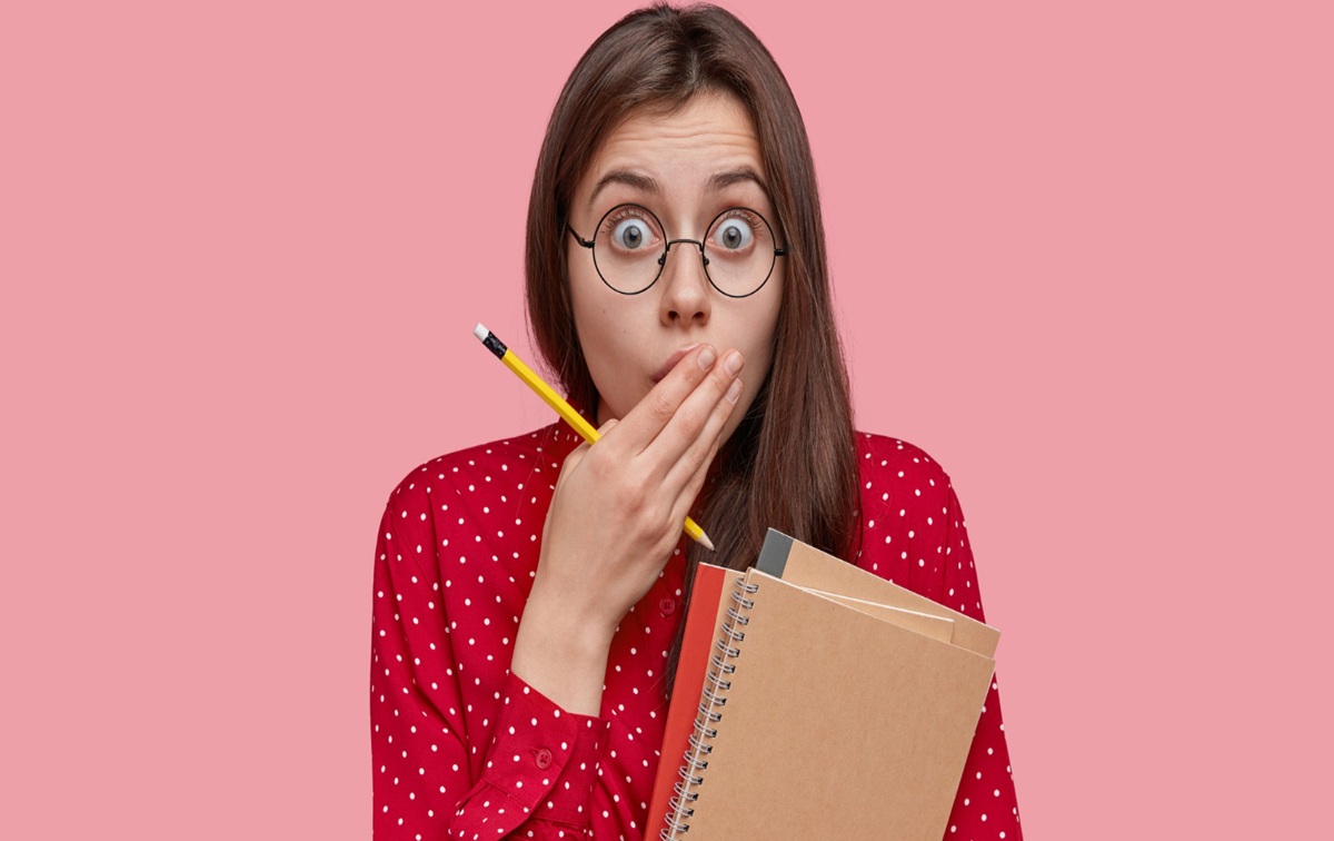 Mulher com expressão surpresa segurando caderno, simbolizando um erro comum de português.