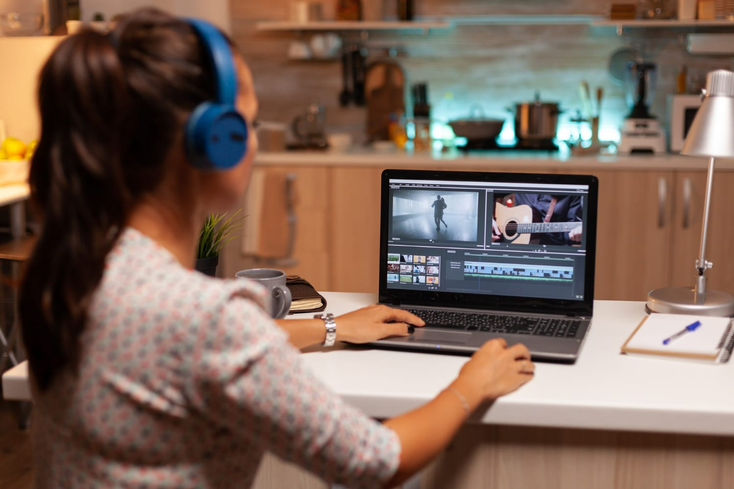 Mulher editando vídeo com fones de ouvido, usando laptop em ambiente moderno e aconchegante.