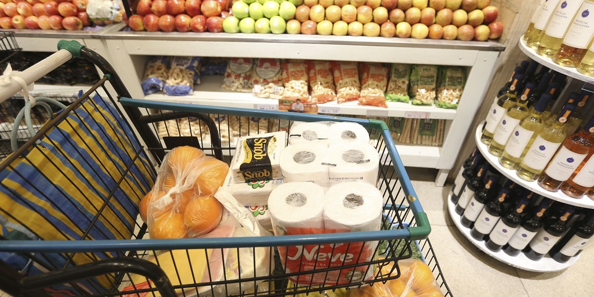 Carrinho de compras no supermercado, com diversos produtos expostos nas prateleiras.