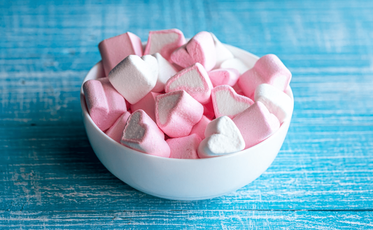 Imagem de marshmallows cor de rosa e branco em uma tigela, representando a doçura e origem do doce.