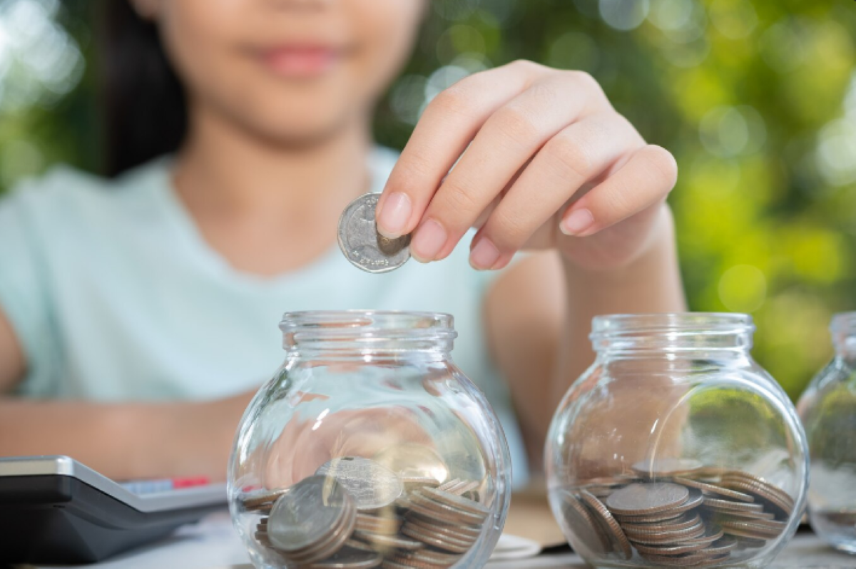 Pessoa colocando moedas em potes de vidro, representando economia e valorização de moedas antigas