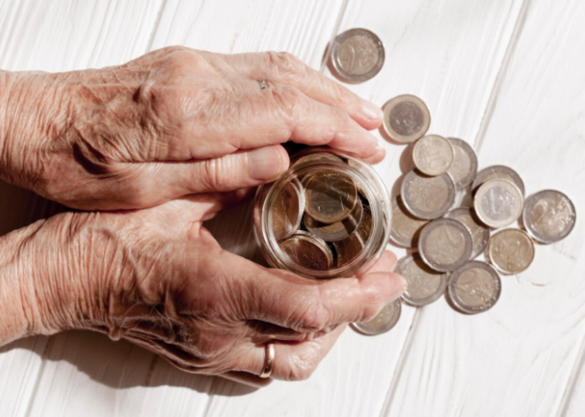 Mãos idosas segurando pote de moedas sobre mesa de madeira