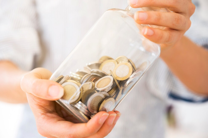 Pessoa segurando pote de vidro cheio de moedas de dois reais