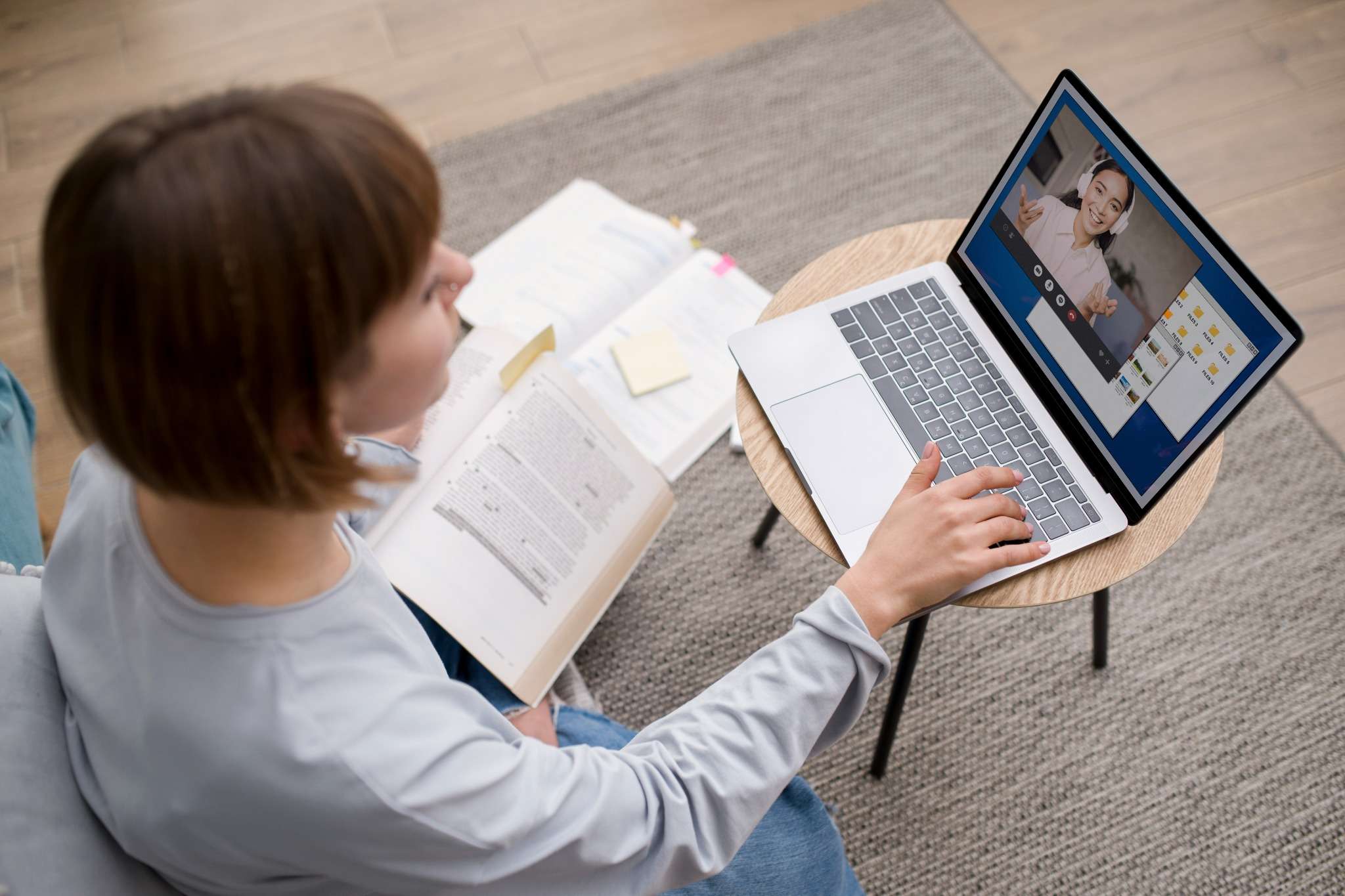 Estudante com livro assiste aula virtual pelo notebook.