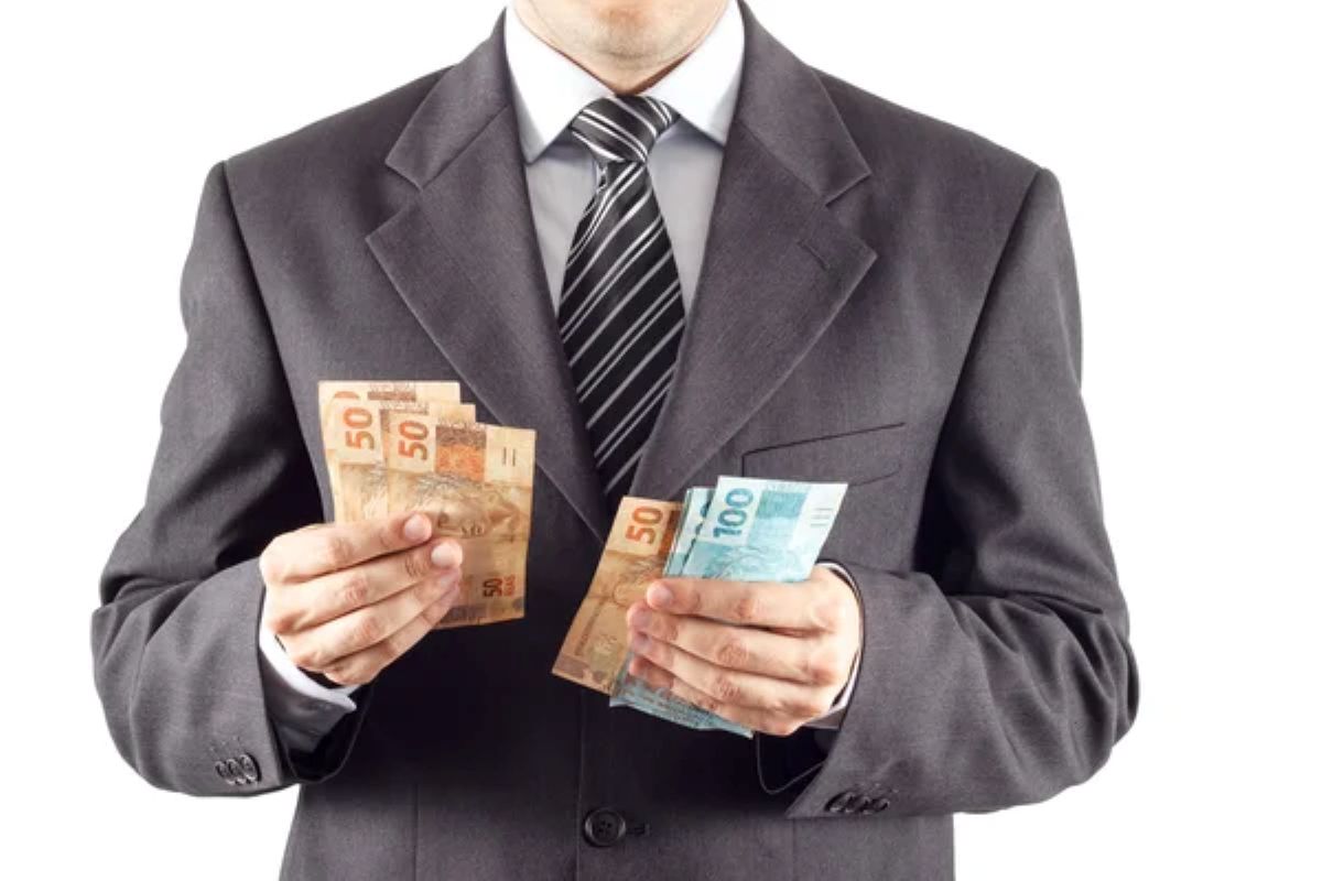 Homem de terno segurando cédulas de R$ 50 e R$ 100, simbolizando o poder de compra de quem recebe R$ 3 mil por mês no Brasil.