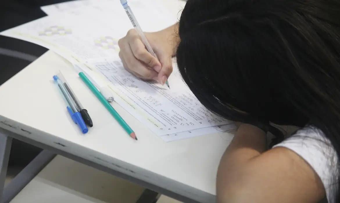 Estudante concentrada preenchendo folha de respostas durante prova do Enem