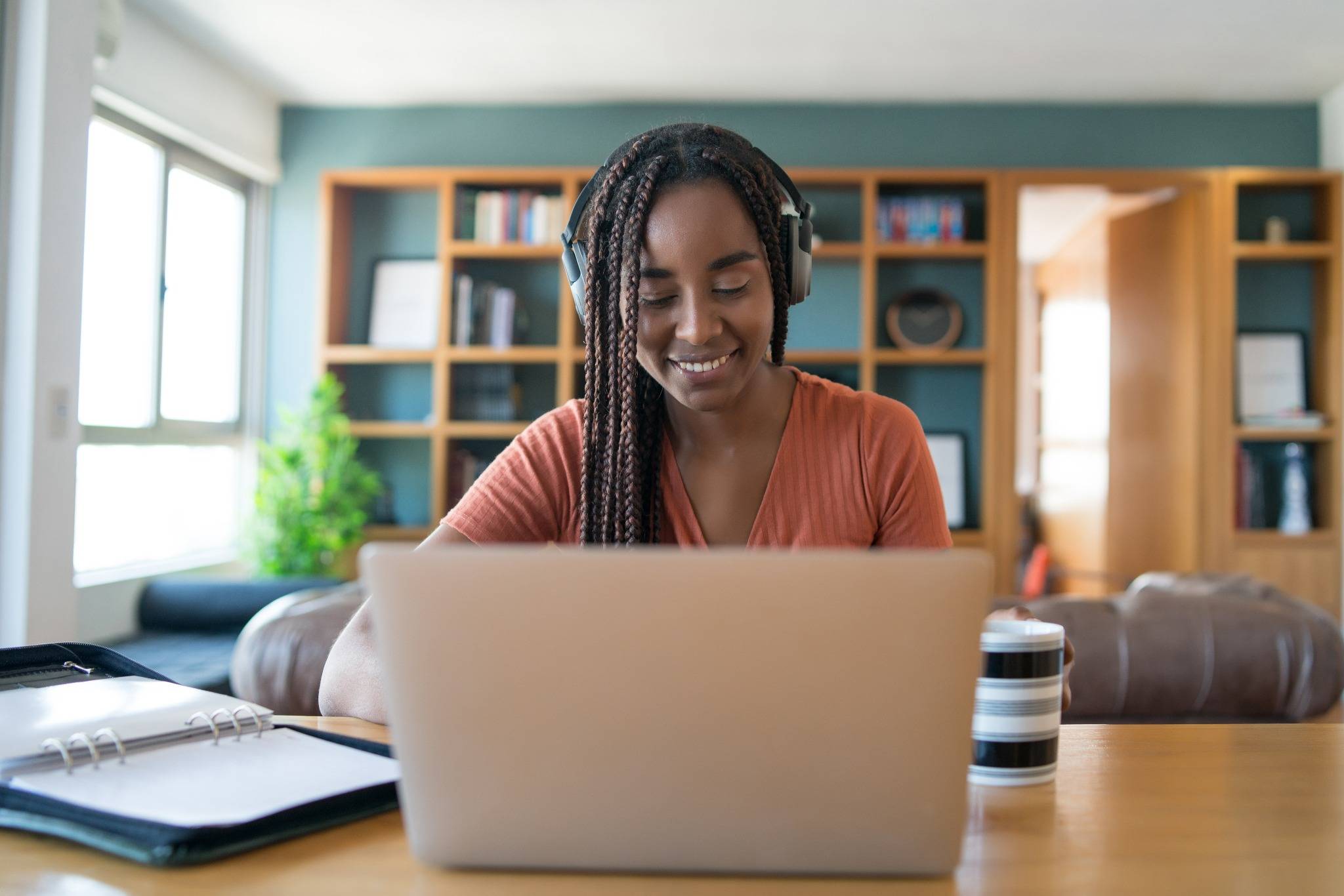 Mulher estudando em casa com fones de ouvido e notebook.