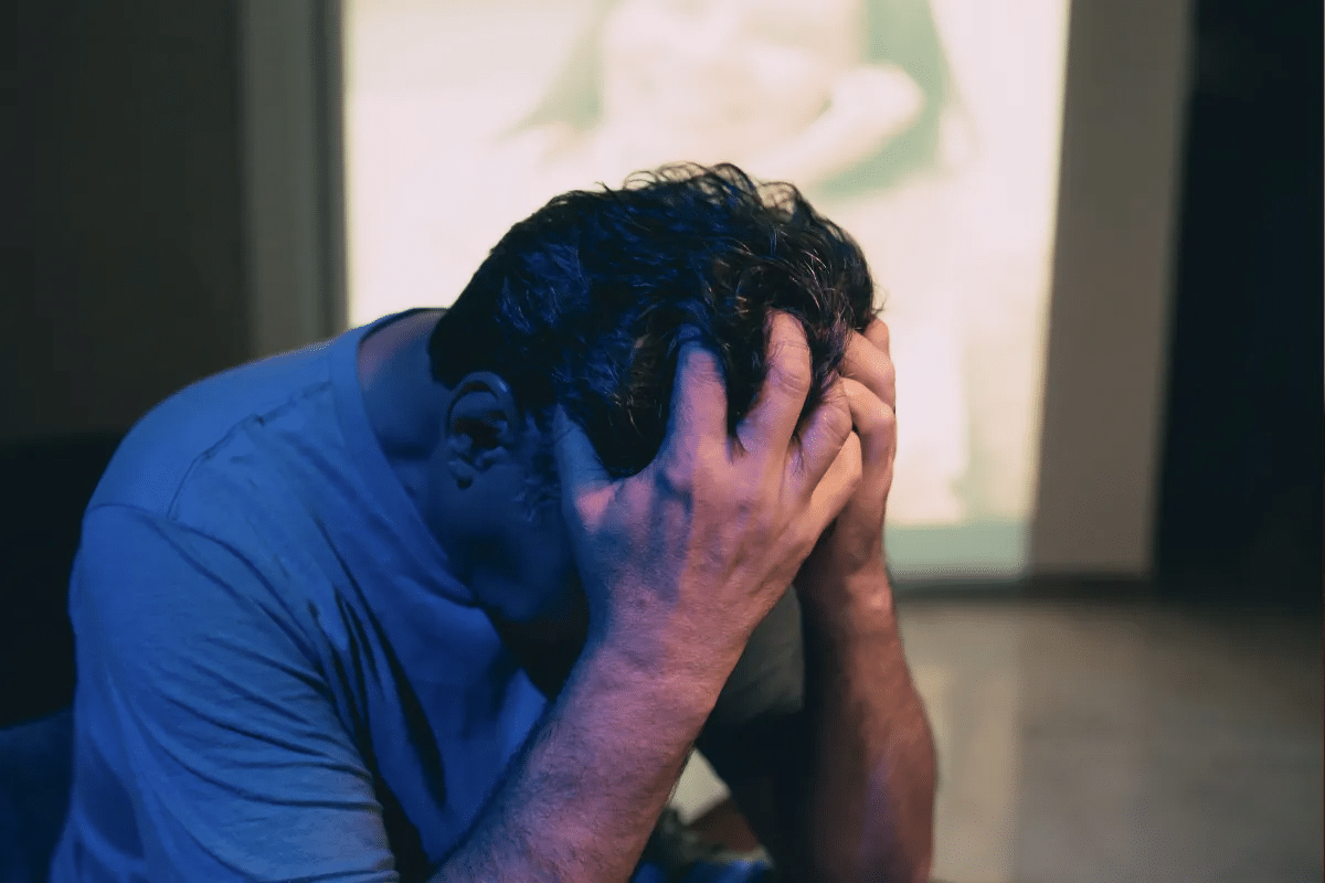 Homem sentado com as mãos na cabeça em momento de estresse ou frustração emocional.