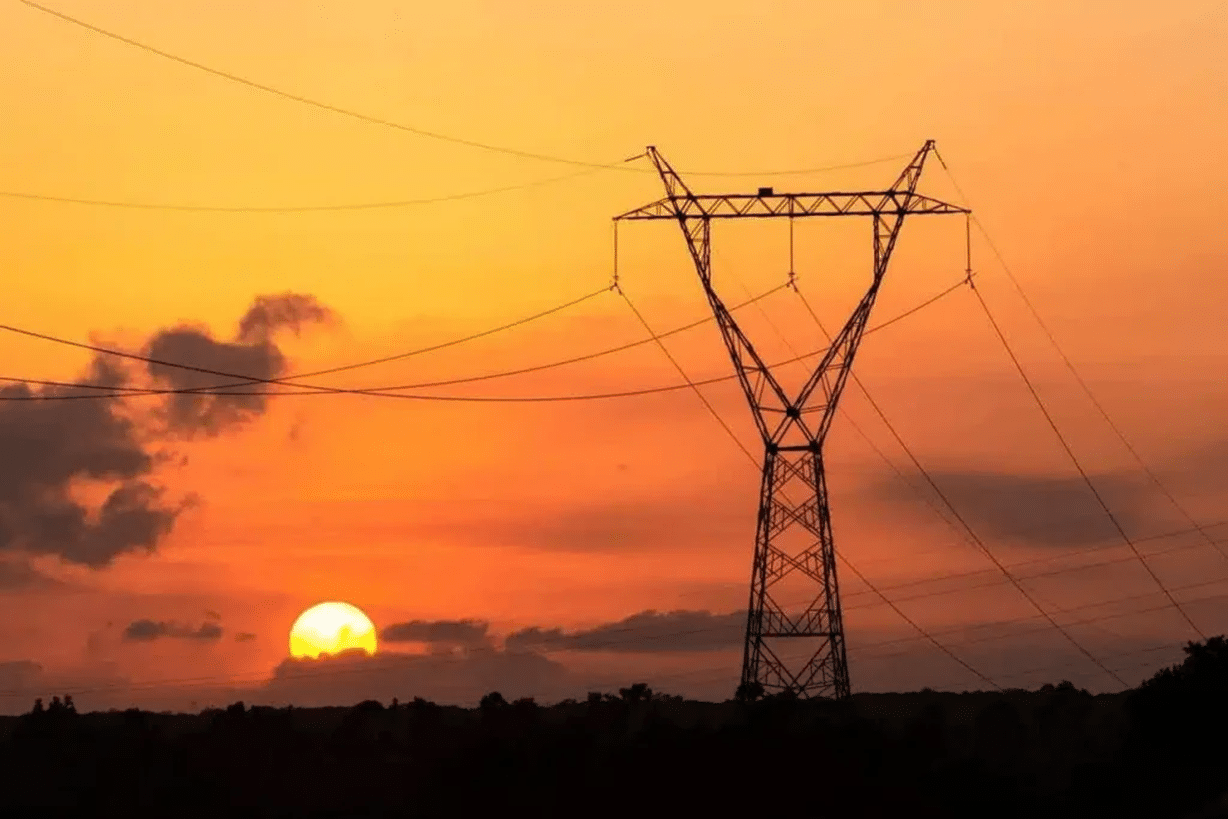Imagem de uma torre de transmissão de energia elétrica ao pôr do sol, simbolizando a mudança no horário de verão.