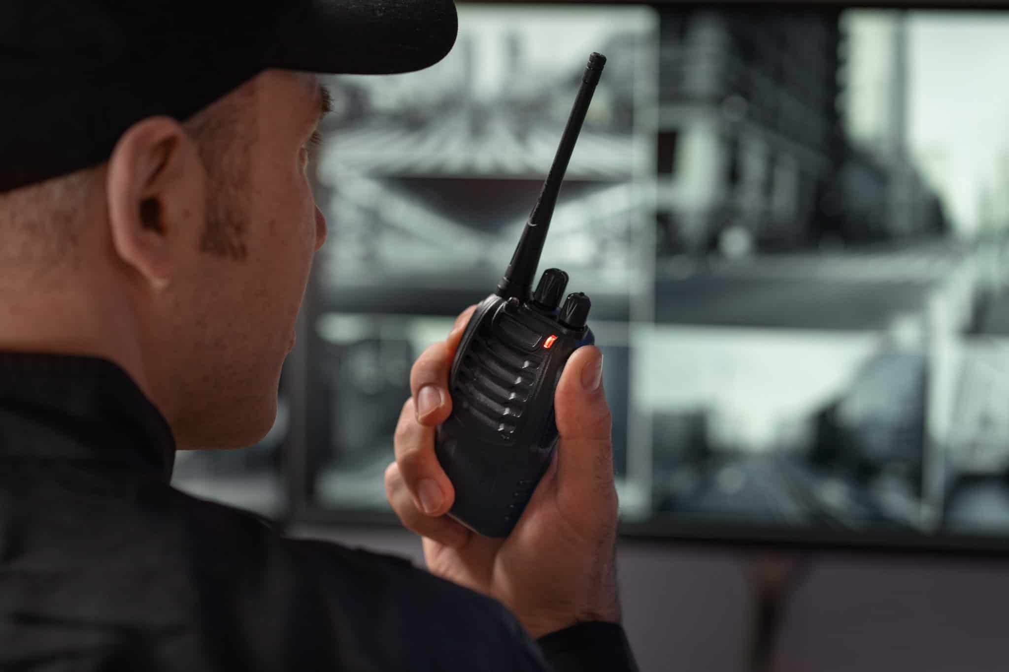 Segurança utilizando rádio comunicador enquanto monitora câmeras de vigilância.