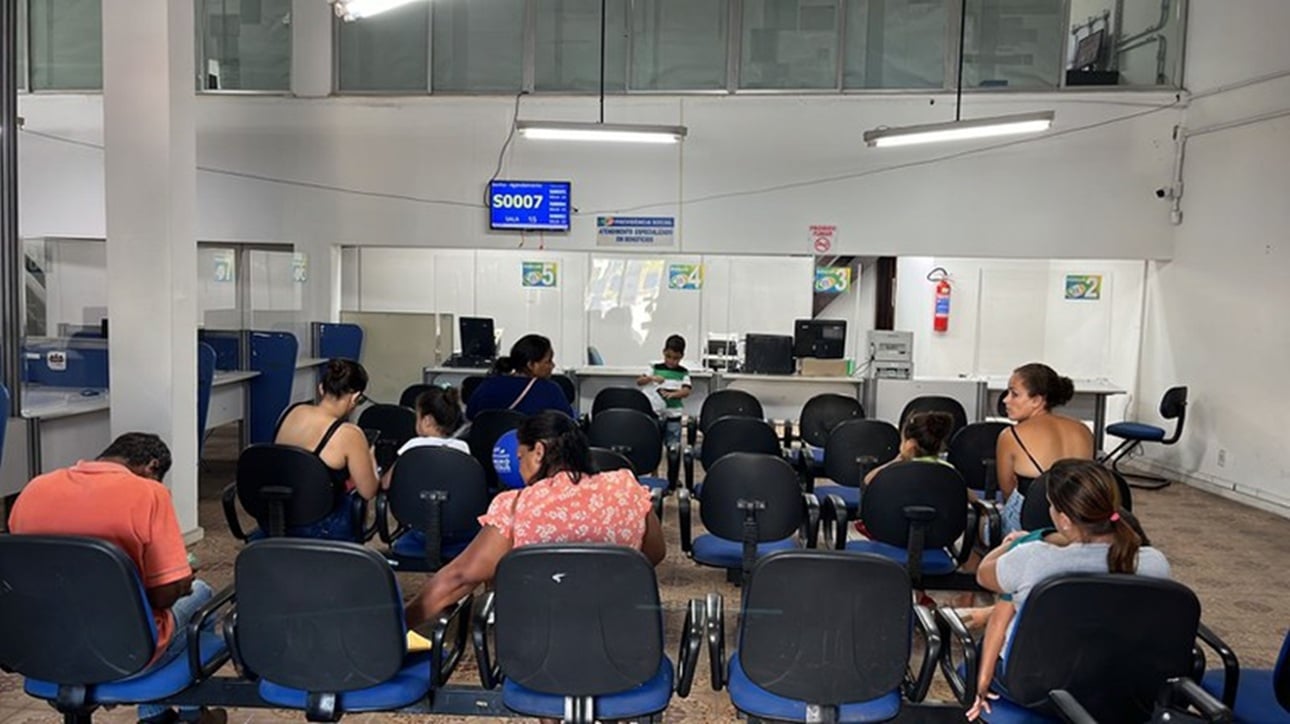 Sala de espera no INSS, com várias pessoas aguardando atendimento.