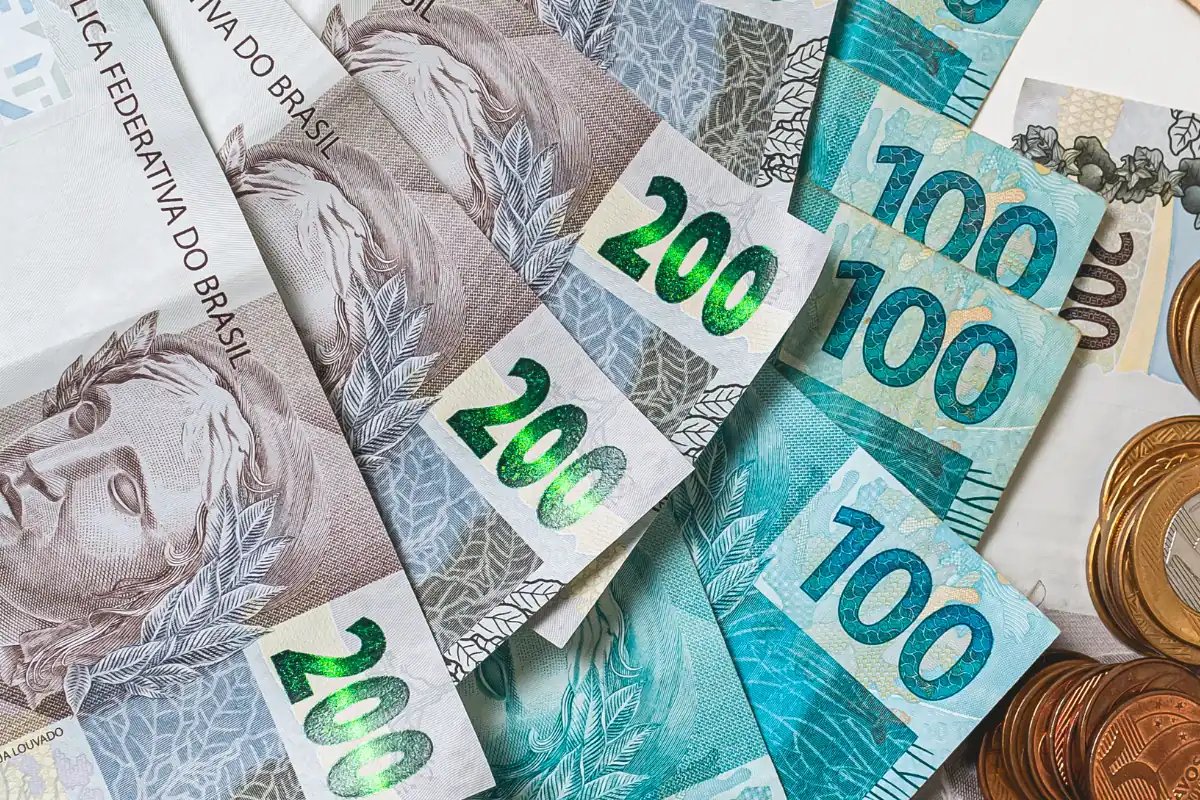 Cédulas de 100 e 200 reais ao lado de moedas brasileiras.