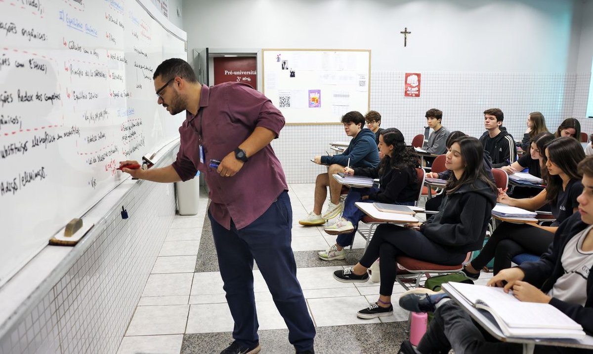 Professor escreve no quadro durante aula preparatória para o Enem com alunos atentos.