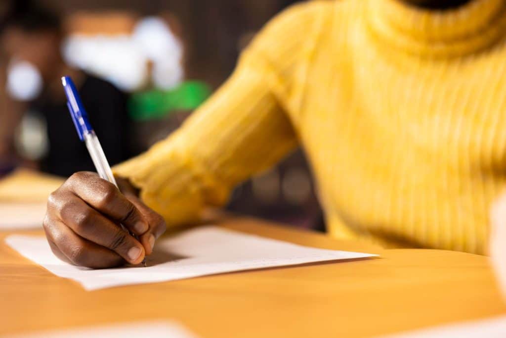 Pessoa escrevendo em papel com caneta em um ambiente de trabalho, representando a inclusão social e a reserva de vagas em concursos públicos.